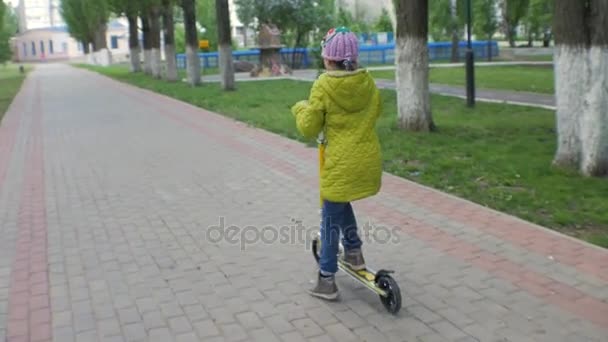 Little girl in green jacket riding a scooter. Shooting Steadicam. - Video