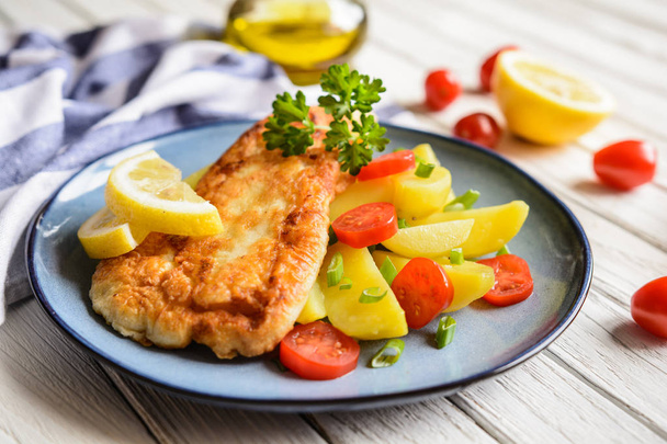 Филе жареной рыбы в тесте, подается с картофелем, помидорами и скаллионом
 - Фото, изображение