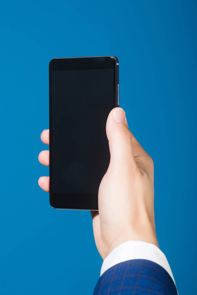 hand with mobile phone on blue background - Photo, Image