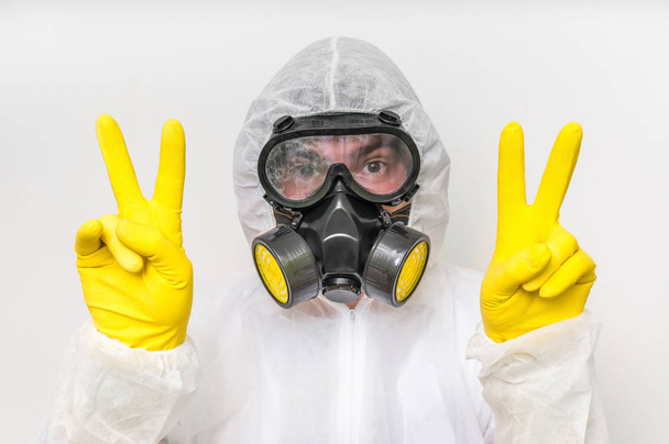 Man in coveralls with gas mask is showing victory symbol - 写真・画像