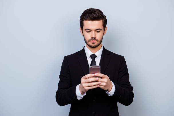 Serious minded man in black suit holding smartphone and typing s - Фото, зображення
