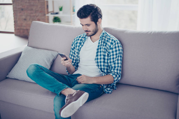 Handsome young smiling man in casual clothes sitting on sofa and - Foto, immagini