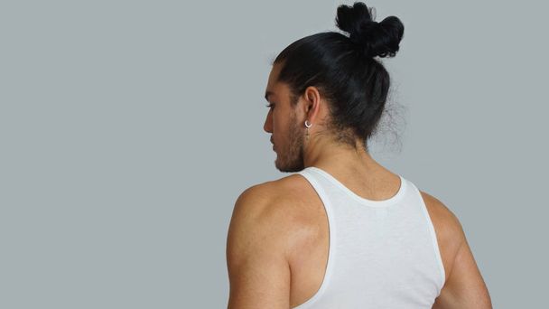 Jeune homme hispanique aux cheveux froncés s'incline en t-shirt blanc sans manches, vu de derrière
 - Photo, image