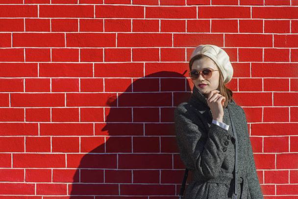 Stylish girl standing at a bright red brick wall - Fotoğraf, Görsel