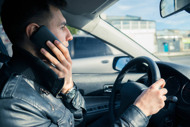 Nuori mies käyttää puhelintaan autoa ajaessaan. Vaarallinen ajaminen
 - Valokuva, kuva