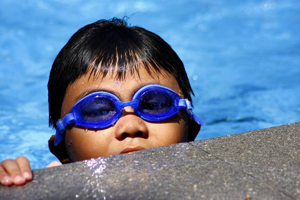 Young kid with swimming goggles in a pool. - Photo, Image