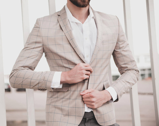portrait of sexy handsome fashion male model man dressed in elegant checkered suit posing outdoors on the street background - Foto, Imagen