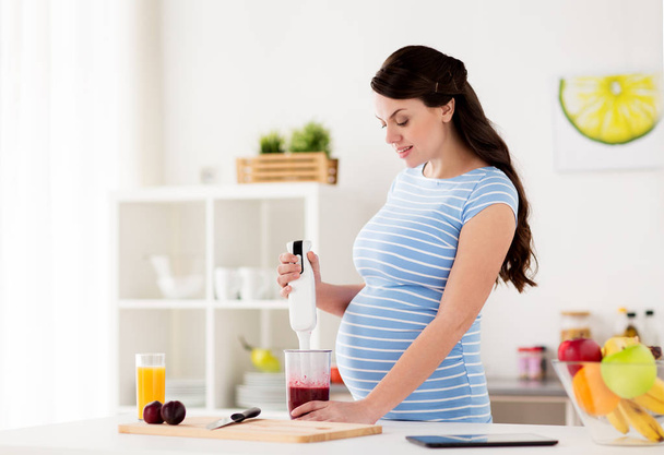 pregnant woman with blender cooking fruits at home - Foto, afbeelding