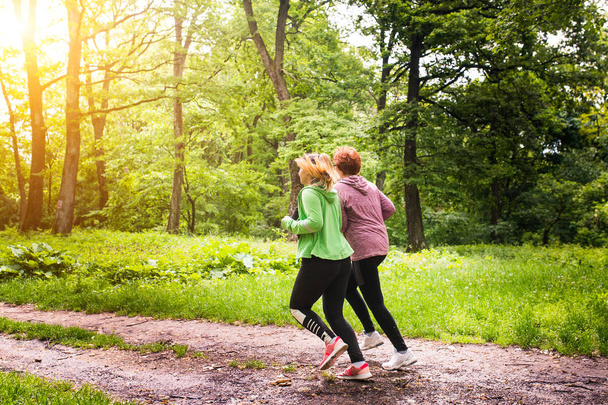 Mother and daughter wearing sportswear and running in forest at  - Φωτογραφία, εικόνα