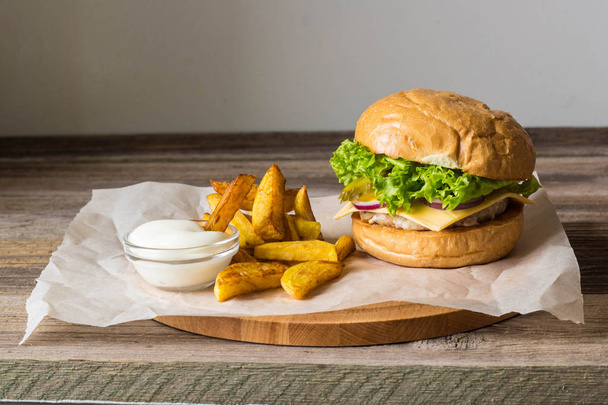 Домашній гамбургер з куркою, цибулею, огірком, салатом та сиром на дерев'яному столі з картопляною картоплею
 - Фото, зображення