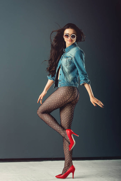 gorgeous girl in a white sunglasses blue jacket red high heel shoes and transparent tights without panties, posing - Фото, изображение