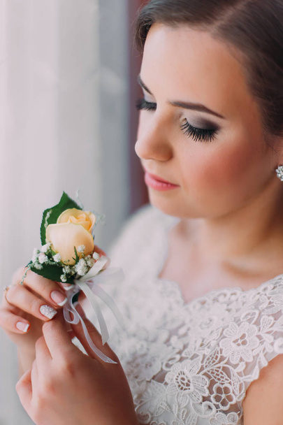 Sensual young bride posing near window holding a cute buttonniere - Photo, image