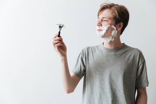 Young man in  shaving foam looking at razor - Zdjęcie, obraz