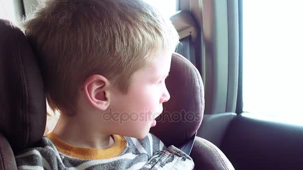 Χαριτωμένο αγόρι σε ένα παιδικό κάθισμα που κοιτάζει έξω από το παράθυρο - Πλάνα, βίντεο