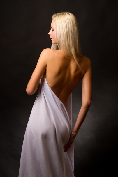 Блондинка топлесс, покрытая белой тканью на черном фоне - Фото, изображение