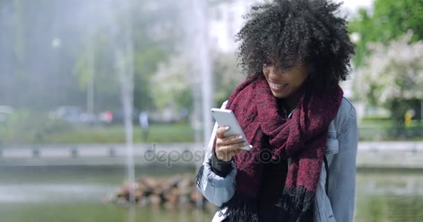 Lächelndes Mädchen mit Telefon am Brunnen - Filmmaterial, Video