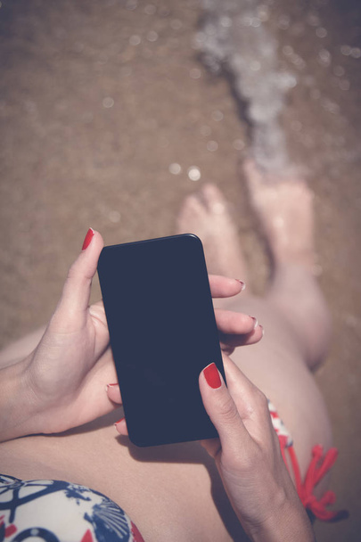 トップダウン ビュー ビーチでの女性両手空白スクリーンのスマート フォンの  - 写真・画像