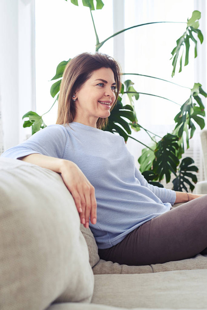 Gyönyörű felnőtt nő ül a világos nappali kanapé - Fotó, kép