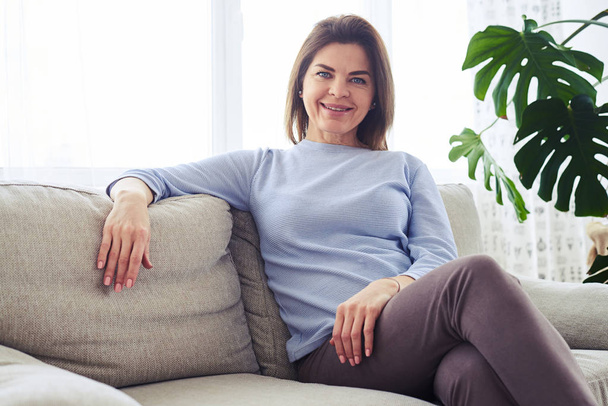 Piękna dla dorosłych kobieta siedzi na kanapie w jasny pokój dzienny - Zdjęcie, obraz