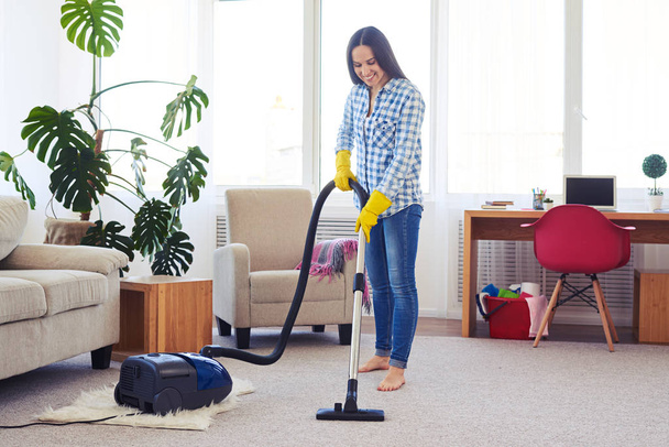 Charming housewife cleaning with vacuum cleaner carpet - Foto, afbeelding