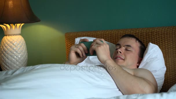 man ligt in bed en gebruik maakt van de toepassing op zijn smartphone. - Video