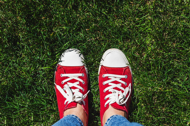 Legs in old red sneakers on green grass. View from above. The co - Photo, Image