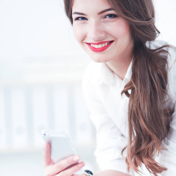 Businesswoman sending message with smartphone in office - Zdjęcie, obraz