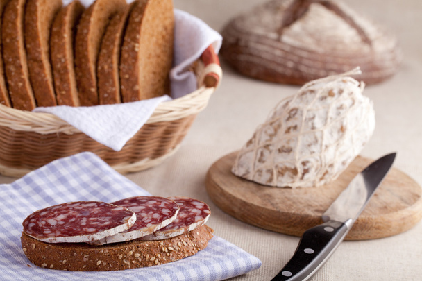 Mesa de cocina servida, sándwich en servilleta, salami, cesta de pan, s
 - Foto, imagen