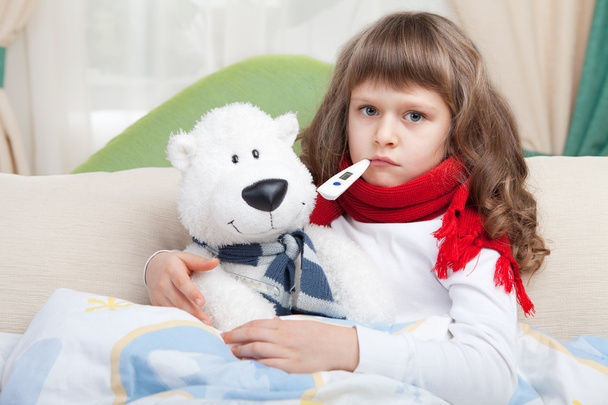 Маленька хвора дівчинка з термометром обіймає іграшкового ведмедя в ліжку
 - Фото, зображення