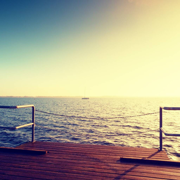 Holzbrücke am Meer bei Sonnenuntergang. windstille Witterung, friedlicher ruhiger Tag in der Bucht.  - Foto, Bild