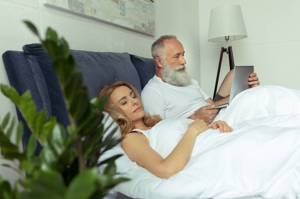Ζευγάρι ώριμο στο κρεβάτι με φορητό υπολογιστή  - Φωτογραφία, εικόνα