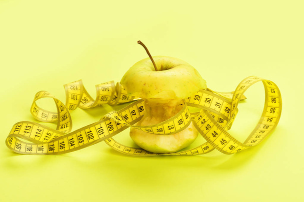 Apple surrounded by measure tape on yellow background - Φωτογραφία, εικόνα