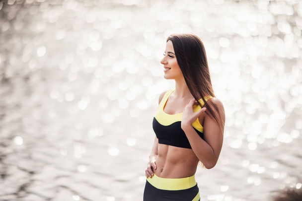 junge Fitness-Frau steht vor Training im Park vor Seeblick-Hintergrund - Foto, Bild
