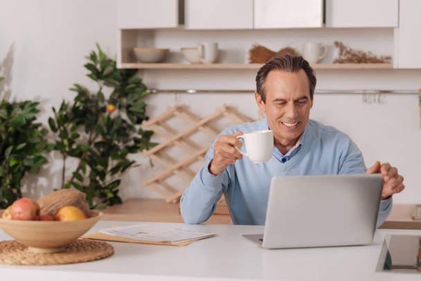 Joyful aging man using laptop at home - Valokuva, kuva