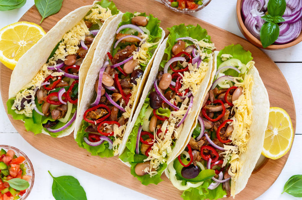 Tacos is a traditional Mexican dish. Tortilla stuffed with chicken, bell and hot peppers, beans, lettuce, cheese, blue onion with salsa sauce on white wooden background. - Fotoğraf, Görsel