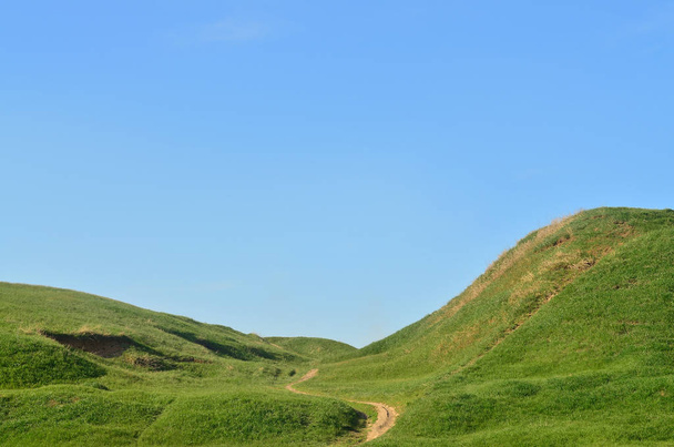 Krajina s prošlapanou cestu procházející nádherné zelené hornatý terén - Fotografie, Obrázek