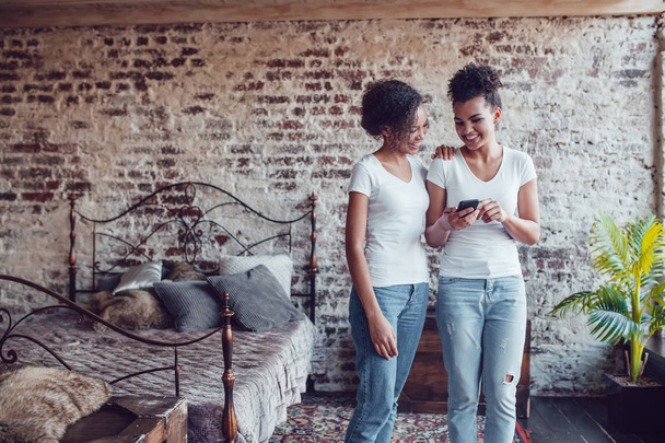 Two attractive African girls at home use smartphone. - Fotó, kép