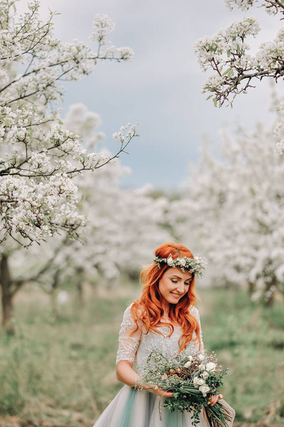 Молодая женщина в роскошном платье стоит и улыбается в цветущем саду
 - Фото, изображение