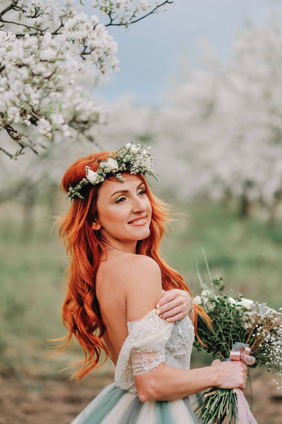Young woman in a luxurious dress is standing and smiling in a blooming garden - Φωτογραφία, εικόνα