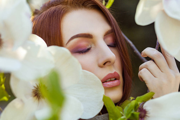 Portrait of young beautiful woman posing among blooming trees with pink eyeshadow. - Fotografie, Obrázek