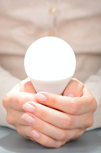 Female hands holding a glowing led bulb - Foto, imagen
