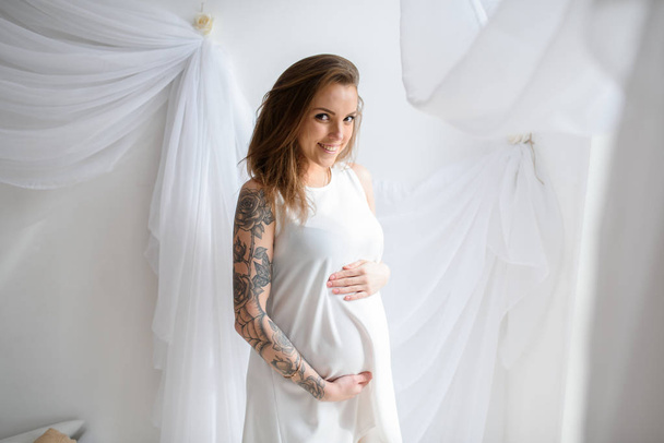 Pregnant girl with tattoo in a white dress. - Zdjęcie, obraz