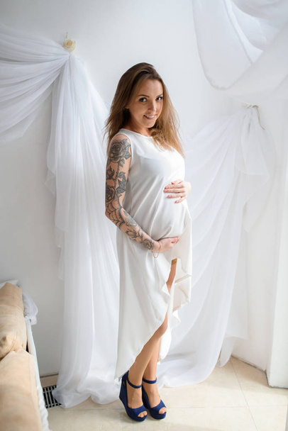 Pregnant girl with tattoo in a white dress. - Valokuva, kuva