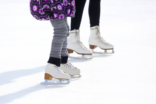 die Beine eines Erwachsenen und eines Kindes beim Schlittschuhlaufen auf der Eisbahn - Foto, Bild