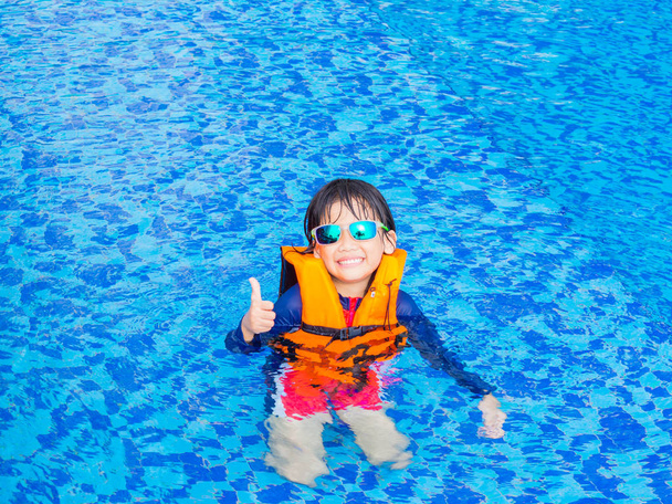 fröhlicher kleiner Junge mit orangefarbener Schwimmweste hat Spaß und genießt im Schwimmbad - Foto, Bild