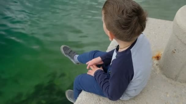 小さな男の子 dangles 彼側の脚に座っている桟橋. - 映像、動画