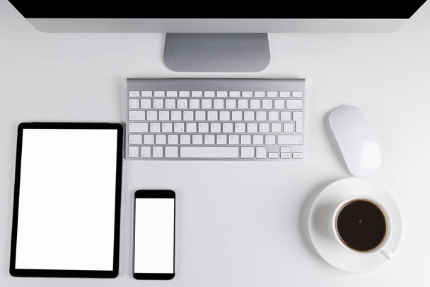 Mesa de oficina con tableta y teléfono inteligente, teclado y ratón inalámbrico, taza de café, cuaderno de espacio de copia. pantalla vacía
 - Foto, imagen