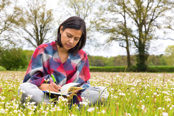 Mulher escrevendo no prado com flores da primavera
 - Foto, Imagem