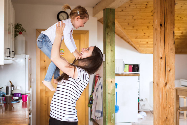 Mother at home lifting little daughter into the air. - Fotografie, Obrázek