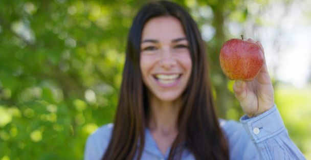 Beautiful young girl holds in hands a fresh ripe red apple, in the background of nature. Concepts: biology, bio products, bio ecology, growing fruit, diet, natural clean and fresh product, environment - Фото, зображення